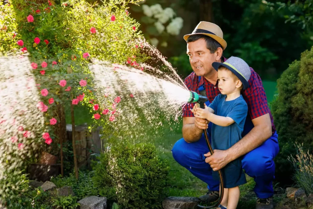 kid watering garden with grandfather